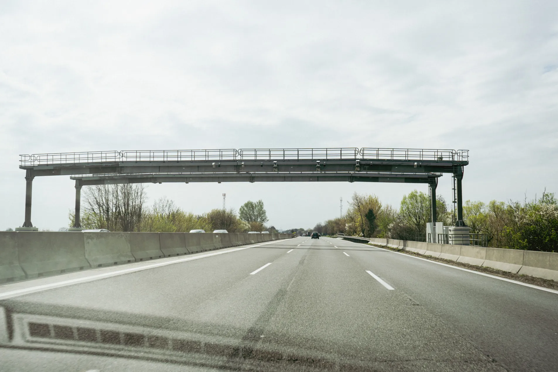 Hungary D2 motorway vignette enforcement gantry with cameras spanning full carriageway with light traffic on wet road and spring trees visible in background, March 2026