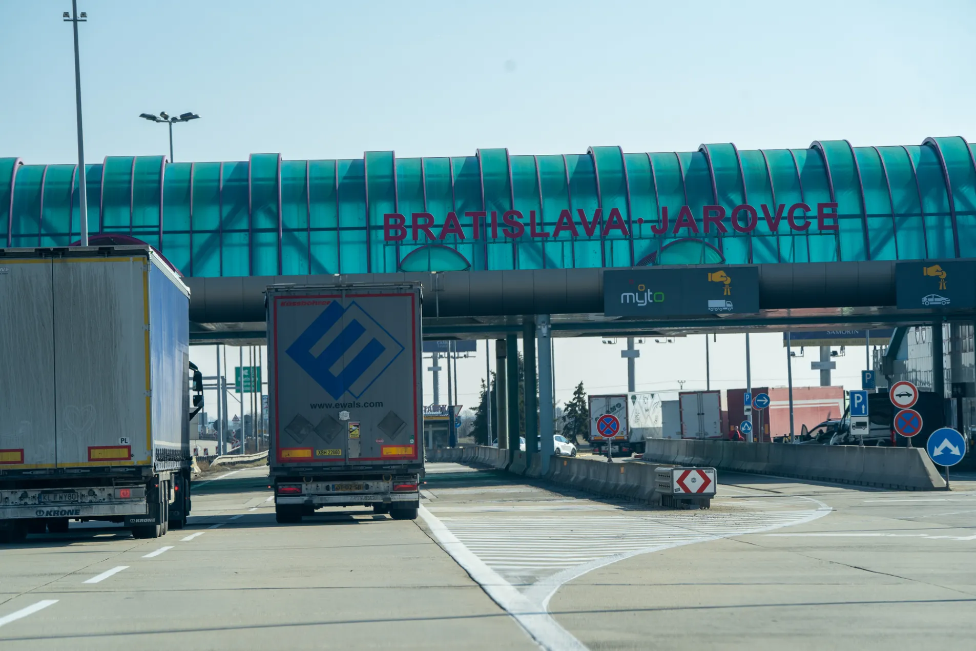 Bratislava-Jarovce border crossing between Slovakia and Austria with trucks passing under teal canopy, Myto toll system signs visible for heavy vehicles, February 2026